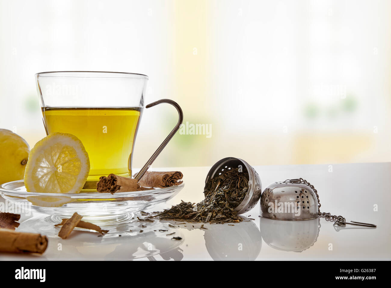 Glass cup green tea with cinnamon stick and lemon on a table in the living room. With metallic strainer Horizontal composition. Stock Photo