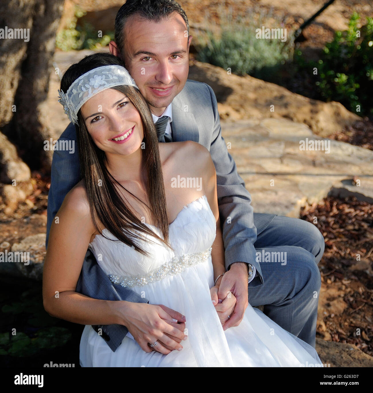 Groom holding the smiling bride sitting on a rock outdoor Stock Photo ...