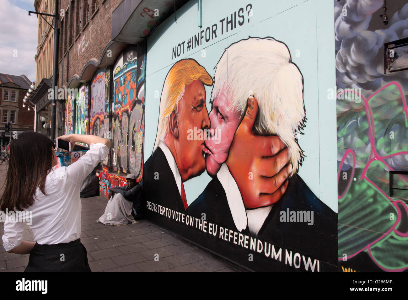 A passerby takes a photo of satirical street art showing Donald Trump kissing Boris Johnson. Stock Photo