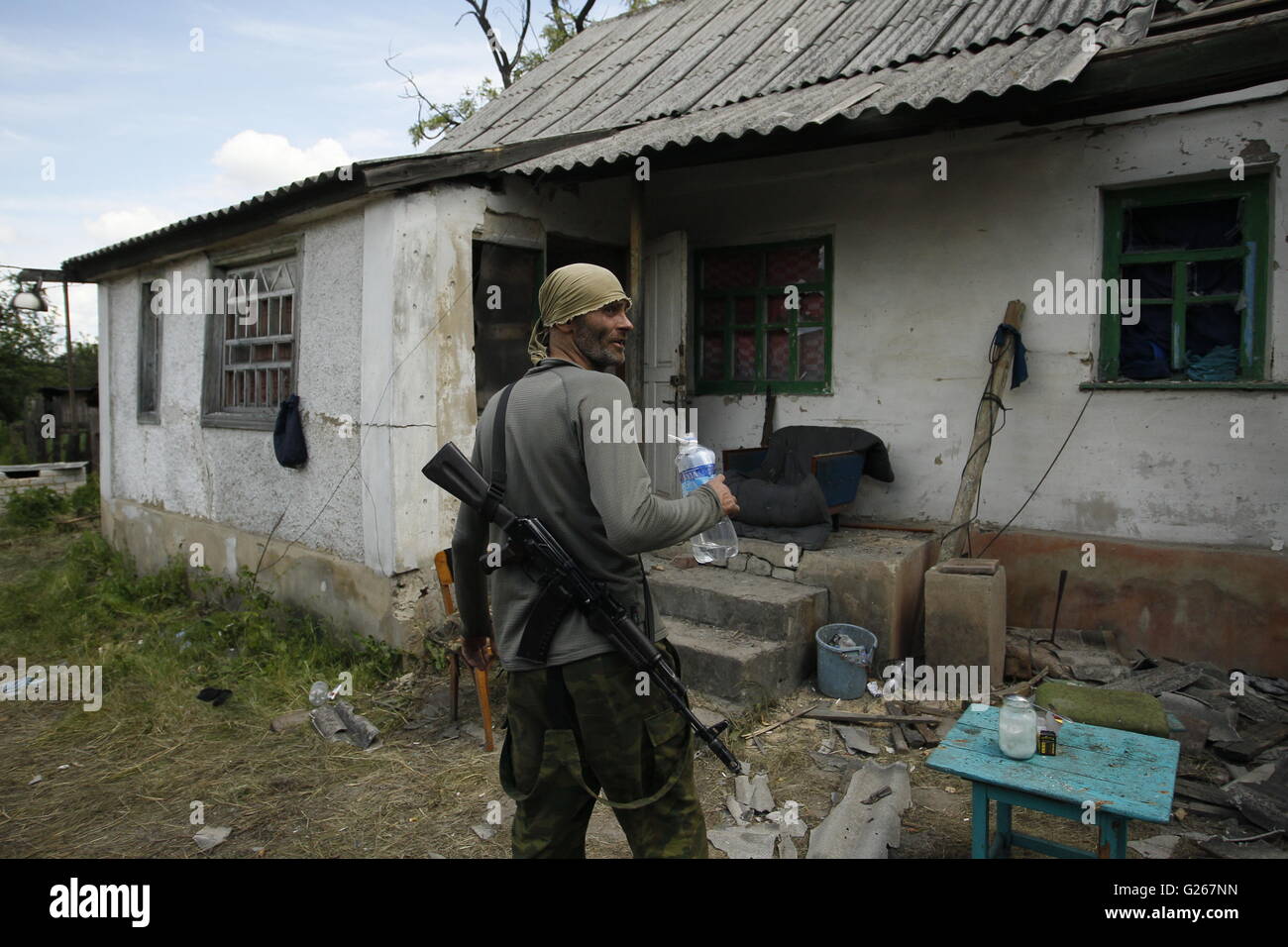 Donetsk, Ukraine. 24th May, 2016. An armed man estimates destroyed home after shelling in rebels controlled Staromykhaylivka village near Donetsk, Ukraine, May 24, 2016. Kremlin spokesman Dmitry Peskov confirmed that the Special Monitoring Mission to Ukraine under the Organization for Security and Co-operation in Europe is being discussed. Credit:  Alexander Ermochenko/Xinhua/Alamy Live News Stock Photo