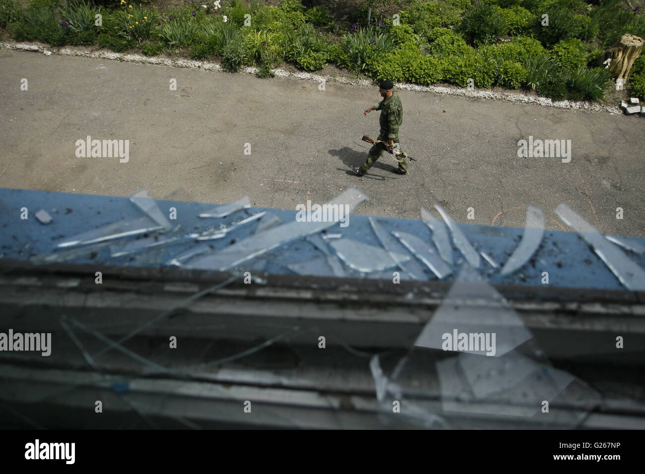 Donetsk, Ukraine. 24th May, 2016. An armed man walks past a damaged window in rebels controlled Staromykhaylivka village near Donetsk, Ukraine, May 24, 2016. Kremlin spokesman Dmitry Peskov confirmed that the Special Monitoring Mission to Ukraine under the Organization for Security and Co-operation in Europe is being discussed. Credit:  Alexander Ermochenko/Xinhua/Alamy Live News Stock Photo