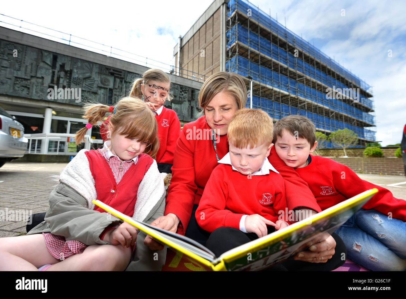 Lewes, UK. 25 May 2016. Teachers and children from Rodmell CE school set up a class outside Council Offices to demonstrate against budget cuts that threaten the school with closure. The pop-up school was set up in the carr park in front of County Hall, Lewes, the East Sussex County Council offices. Pictured s teacher Ms Featherstone reading to children. Credit: Peter Cripps/Alamy Live News Stock Photo