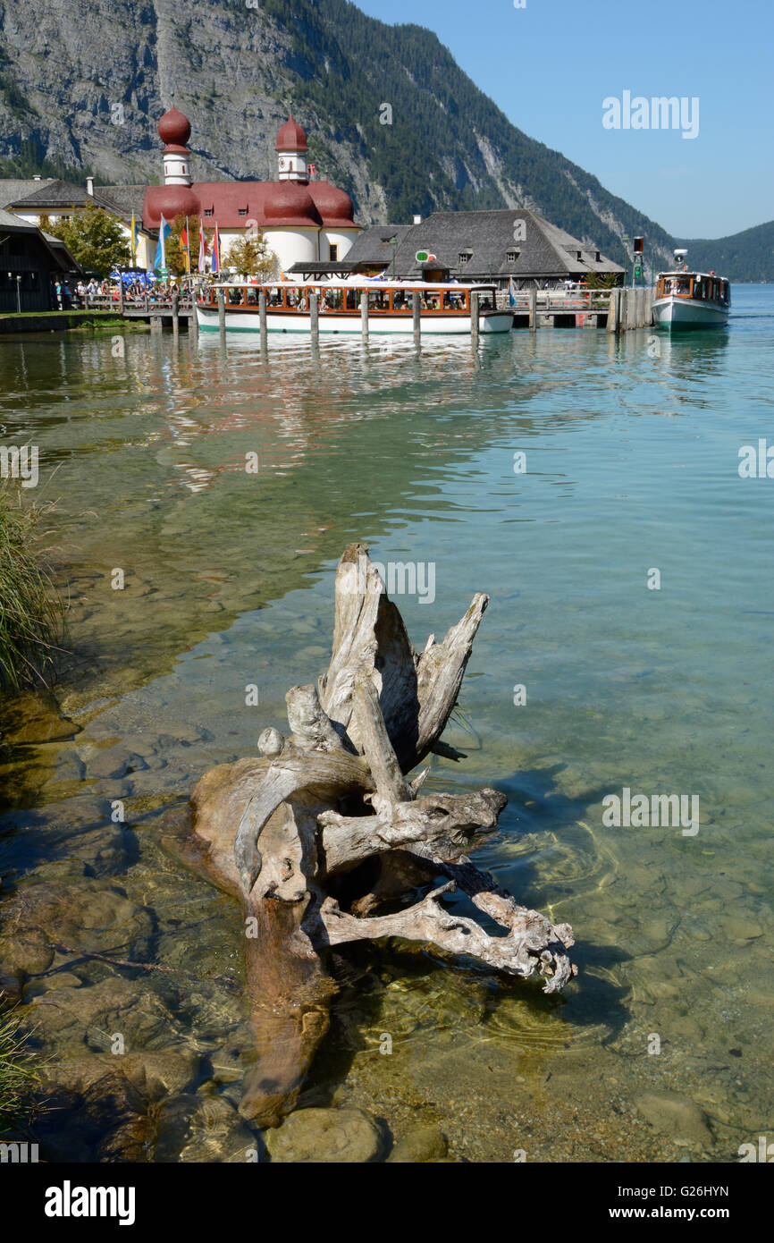 Schonau am Konigssee, Germany - August 30, 2015: Withered tree root, boats and St. Bartholoma church at Koenigssee lake nearby S Stock Photo