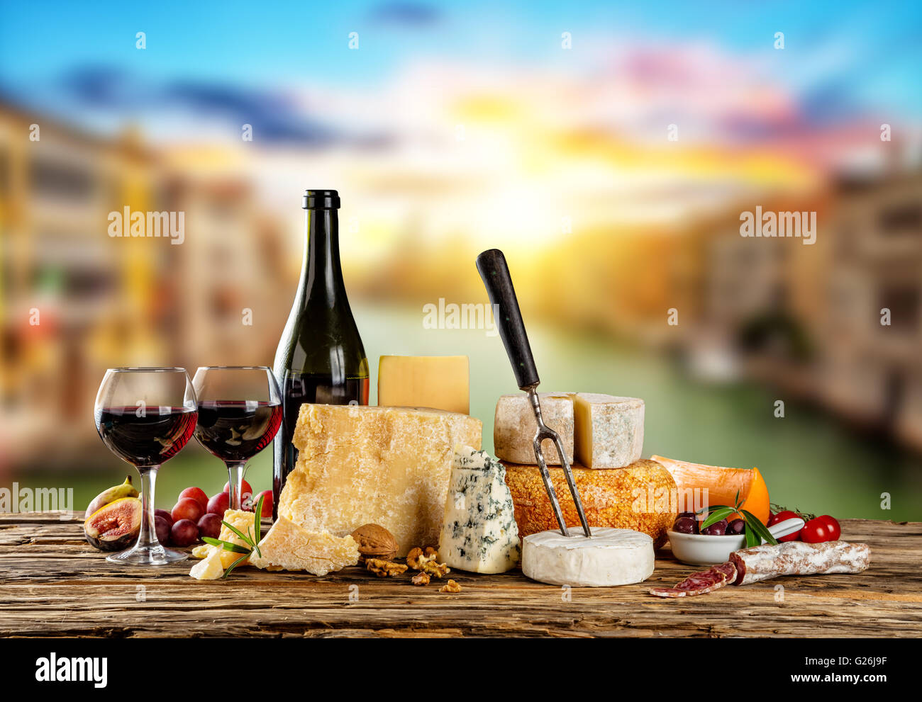 Various types of cheese, glasses and bottle of red wine placed on wooden table, copyspace for text. Blur old town on background Stock Photo