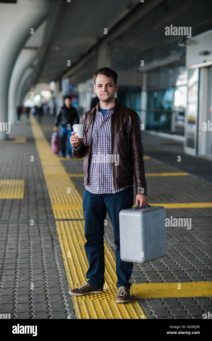 Young attractive man drinking coffee on his way near the airport terminal looking to the camera Stock Photo