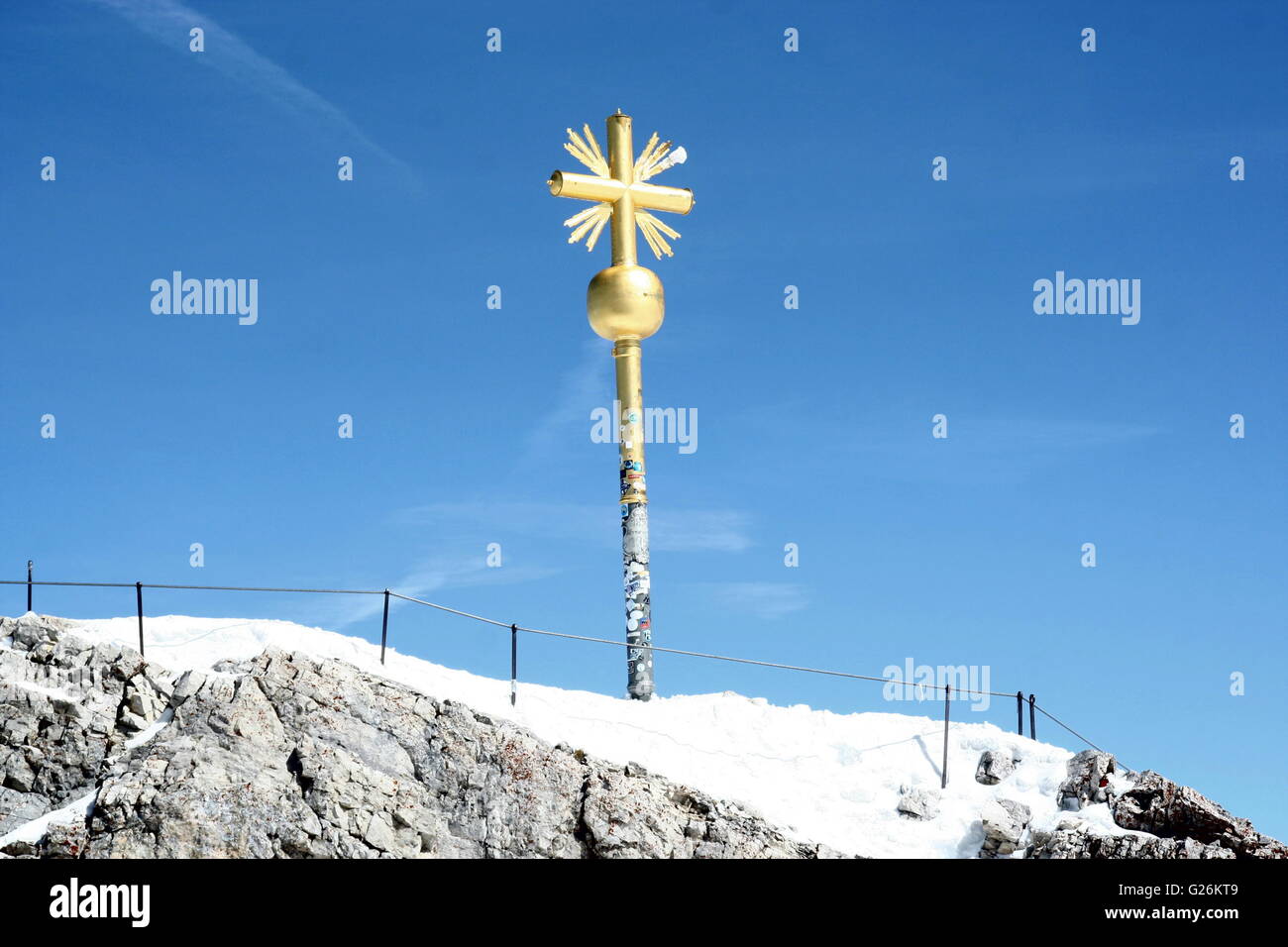 Gold cross marking the summit, Zugspitze, the highest peak in Germany.  The cross stands against a blue sky. Stock Photo