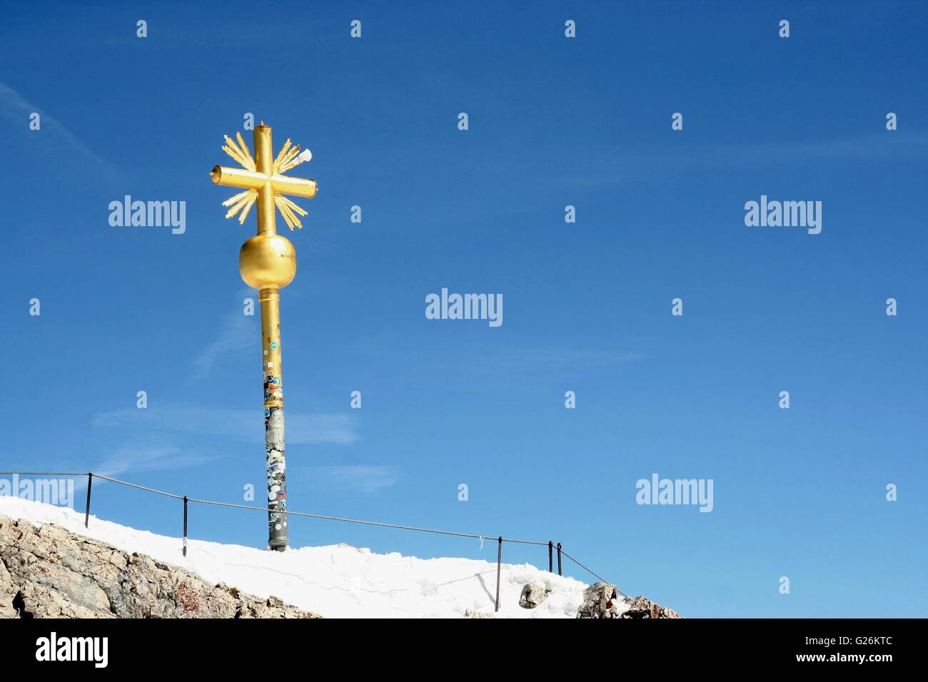 Gold cross marking the summit, Zugspitze, the highest peak in Germany.  The cross stands against a blue sky. Stock Photo