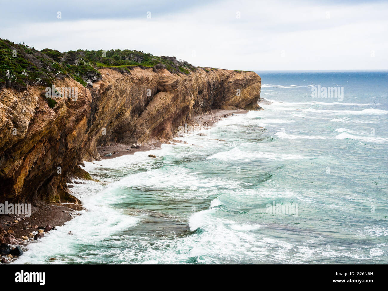 Waves splashing against eroding muddy coastline showing diagonal strata ...
