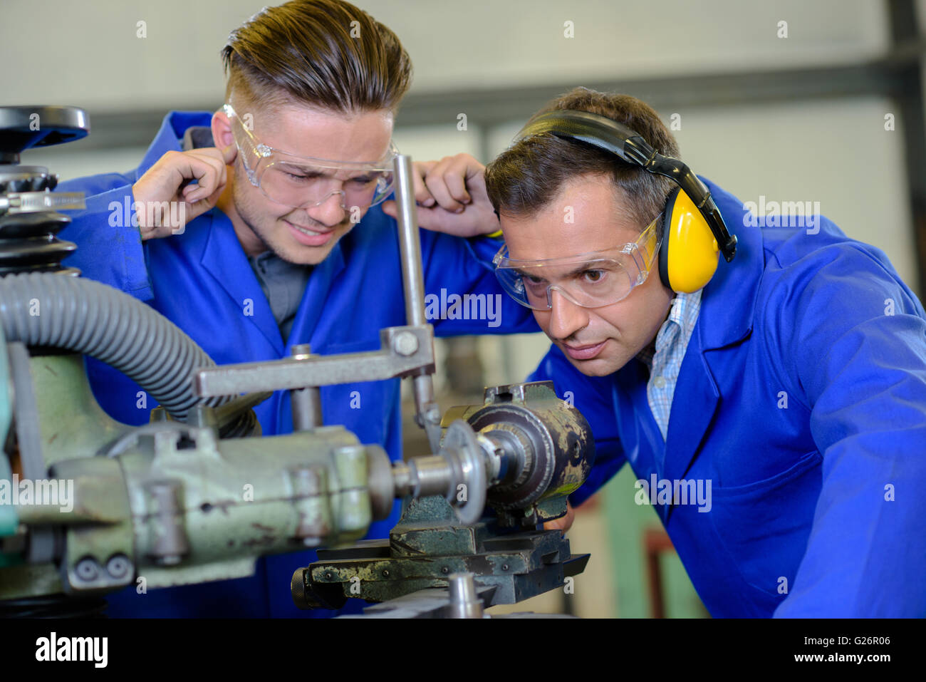 Engineer using machine apprentice with fingers in ears Stock Photo Alamy