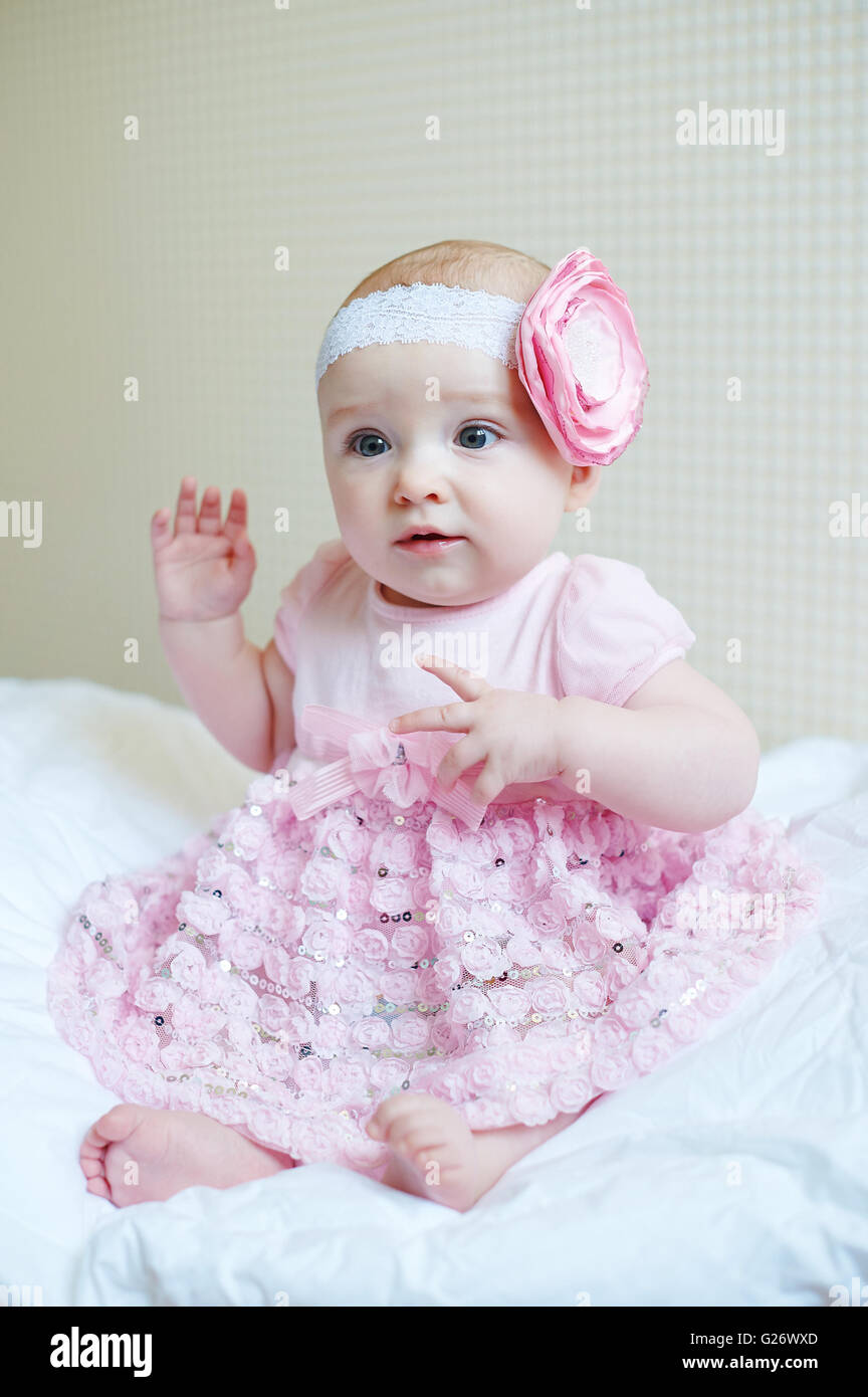 Cute beautiful baby girl sitting on a bed in pink dress Stock Photo