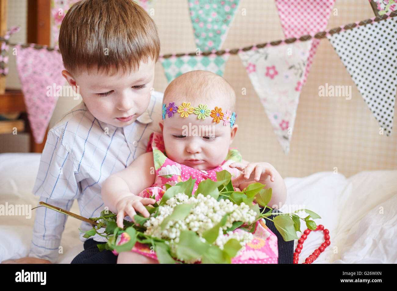 Cute little brother and sister sitting on the bed in their room Stock Photo