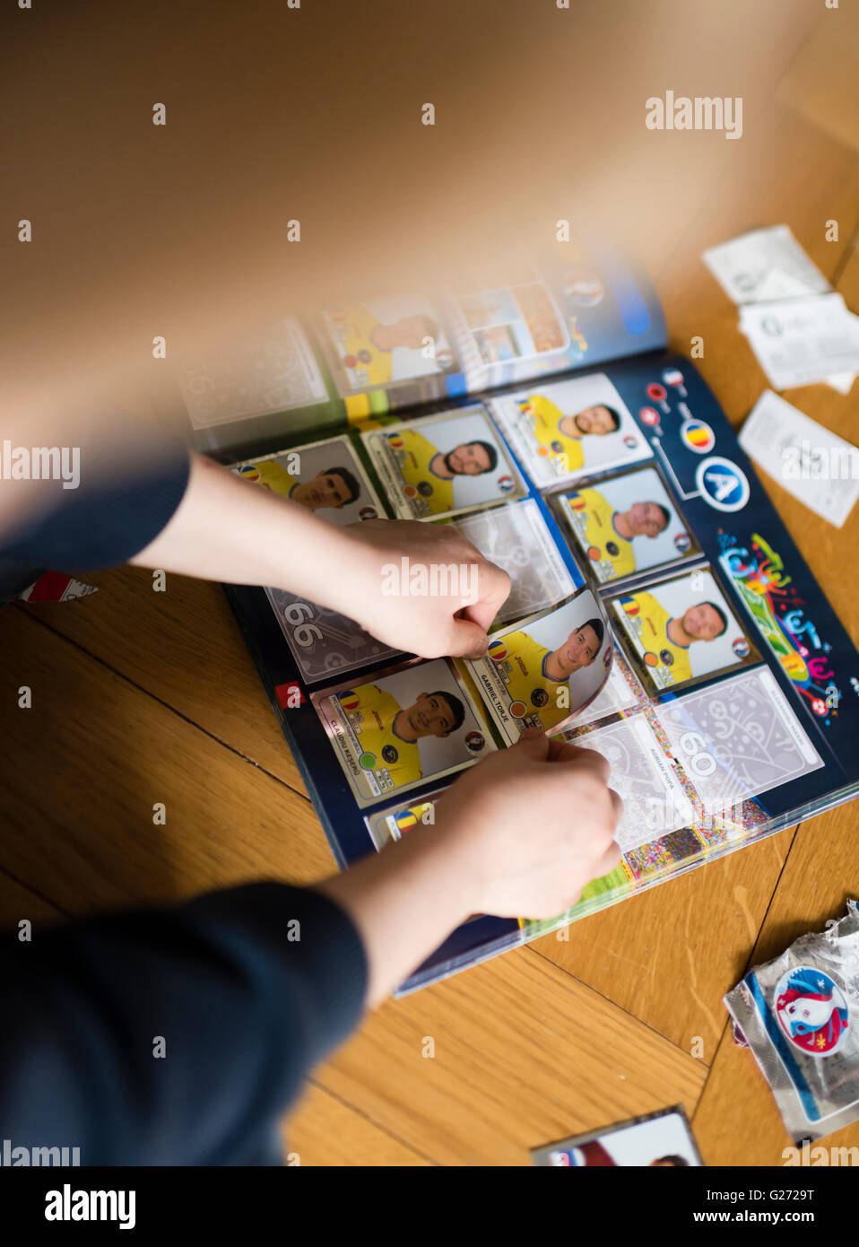An 8 year old boy is pasting UEFA Euro 2016 Panini football trading cards into his sticker collection scrapbook. Stock Photo