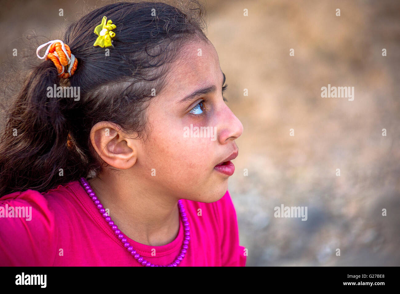 Profile portrait of a nine year old girl in a red dress, red beaded necklace, and pigtails. Stock Photo