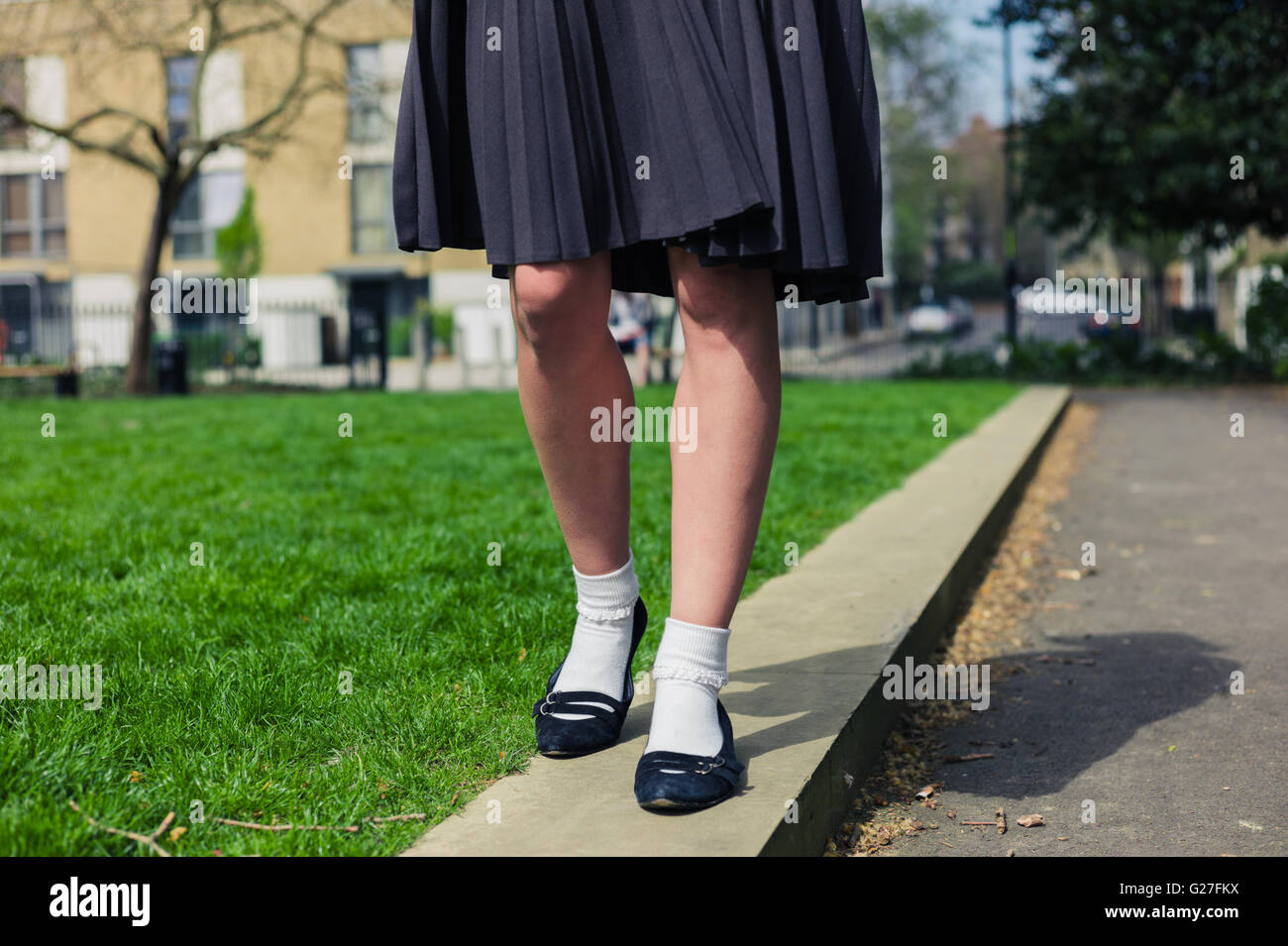 A young woman wearing a skirt is walking in a park by the green grass ...
