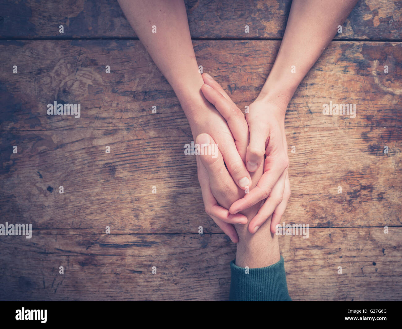 Close up on a man and a woman holding hands at a wooden table Stock Photo