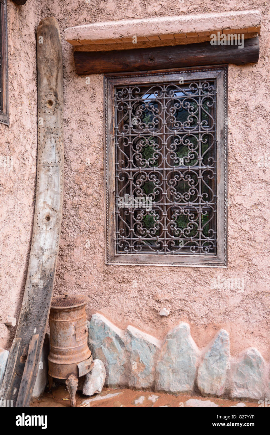 an ornate metal wrought iron grill on a closed Moroccan window in a terracotta coloured wall with a heavy lintel and stone skirting, Morocco Stock Photo