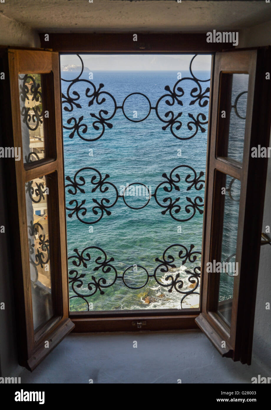 Looking through an ornate wrought iron grill on open Greek window looking out to sea ocean below, Greece Stock Photo