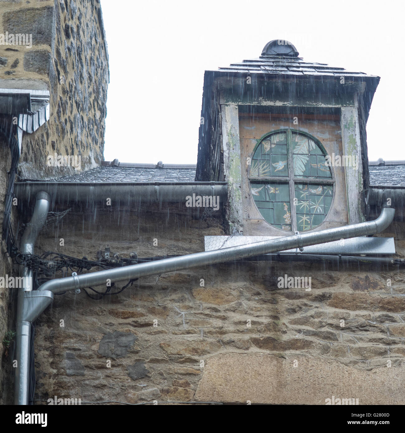 rain falling on an old attic wood and lead roof window and draining down aluminium guttering, Dinan France Stock Photo