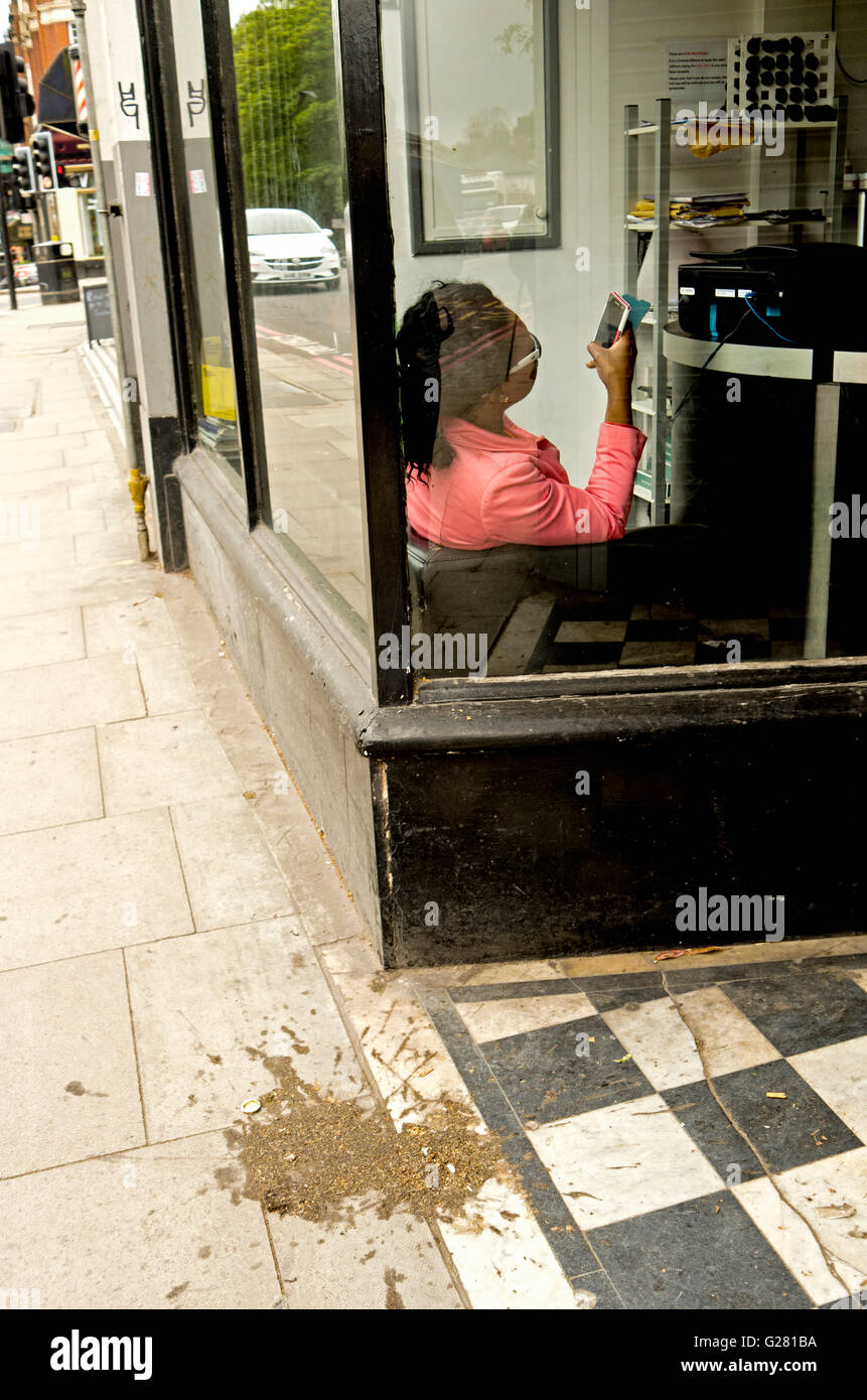 A woman can be seen sitting inside a shop, checking her mobile, whilst outside, a splatter marks the pavement. Stock Photo