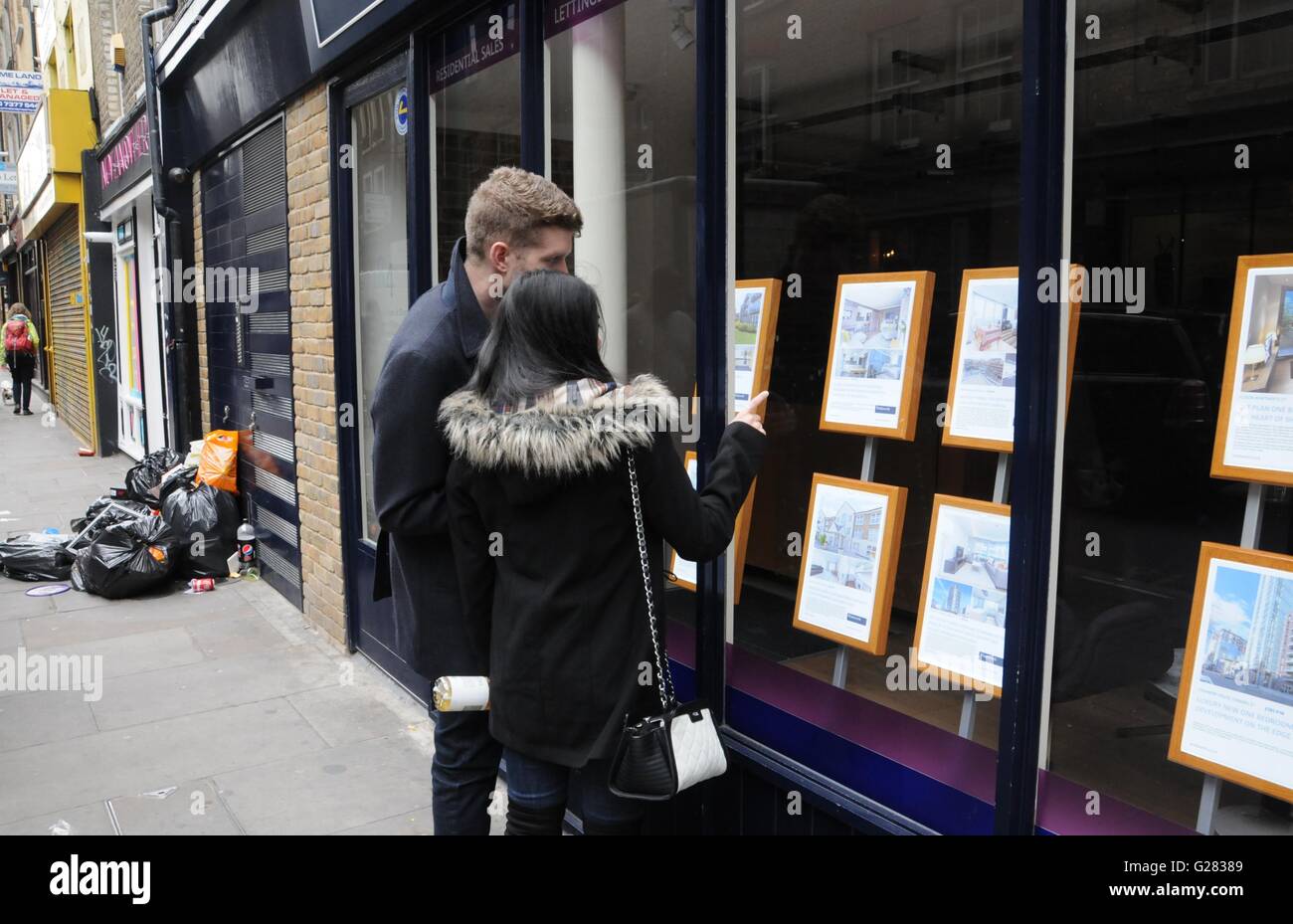 Young couple view property in estate agent's window, in the up and