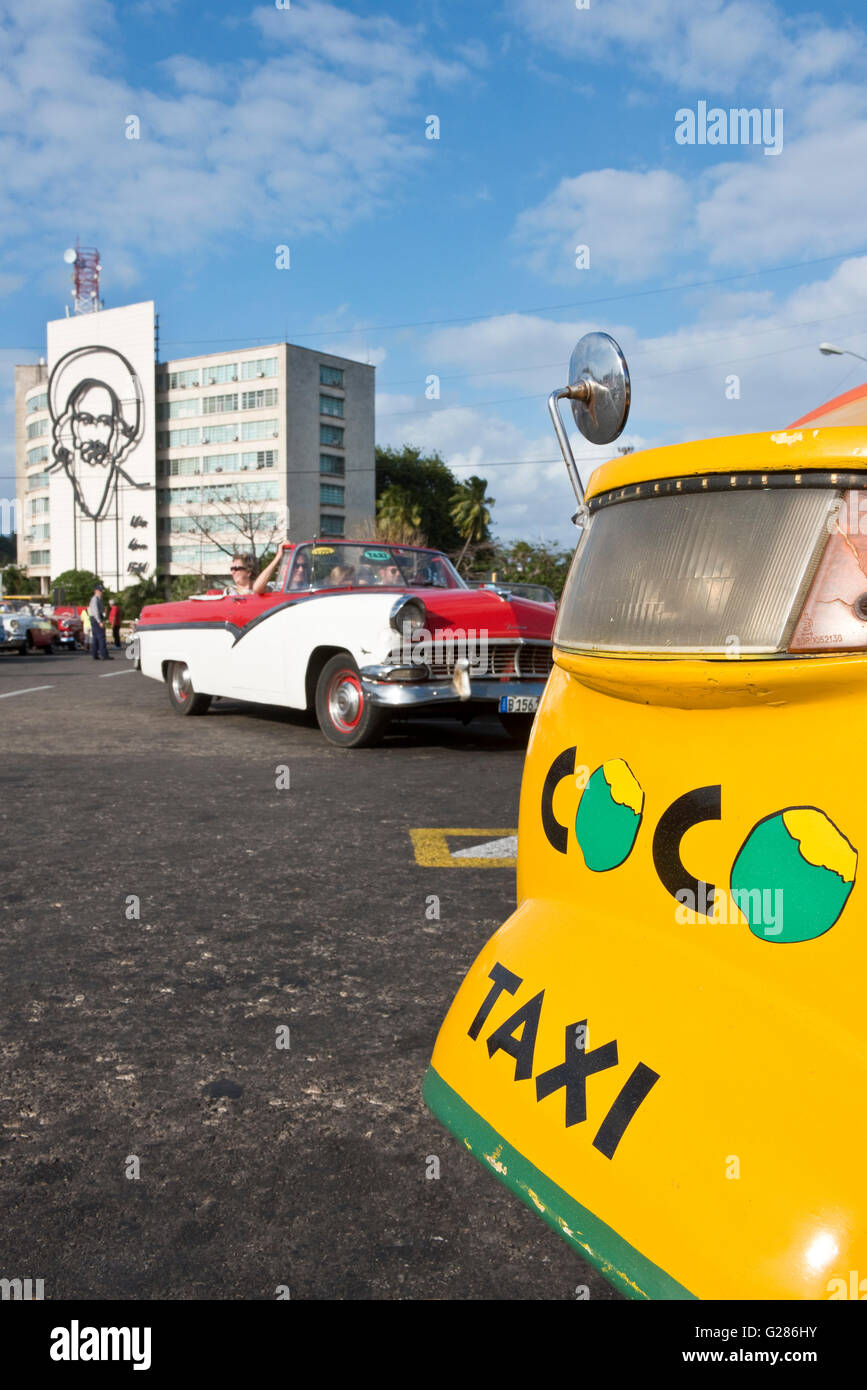 A coco taxi, American 1950's taxi car middle and the image of Camilo Cienfuegos on the building background on revolution Square. Stock Photo