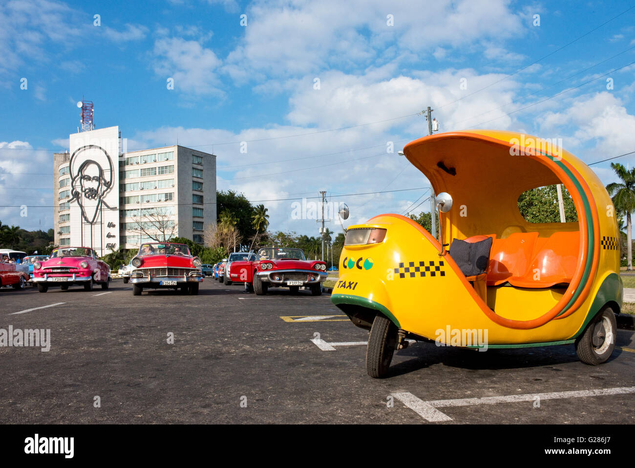 A coco taxi, American 1950's taxis middle and the image of Camilo Cienfuegos on the building background on revolution Square. Stock Photo