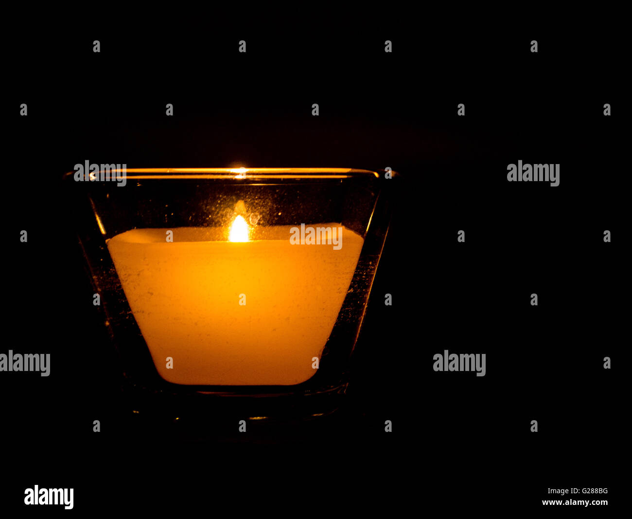 Lit candle in square glass surrounded by darkness Stock Photo Alamy