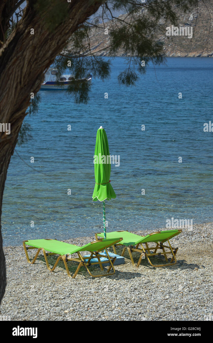 Two empty lime green sun loungers with a closed parasol sun shade on a shingle beach by the water's edge Stock Photo