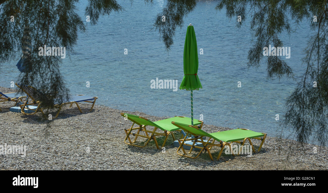 Two empty lime green sun loungers with a closed parasol sun shade on a shingle beach by the water's edge Stock Photo
