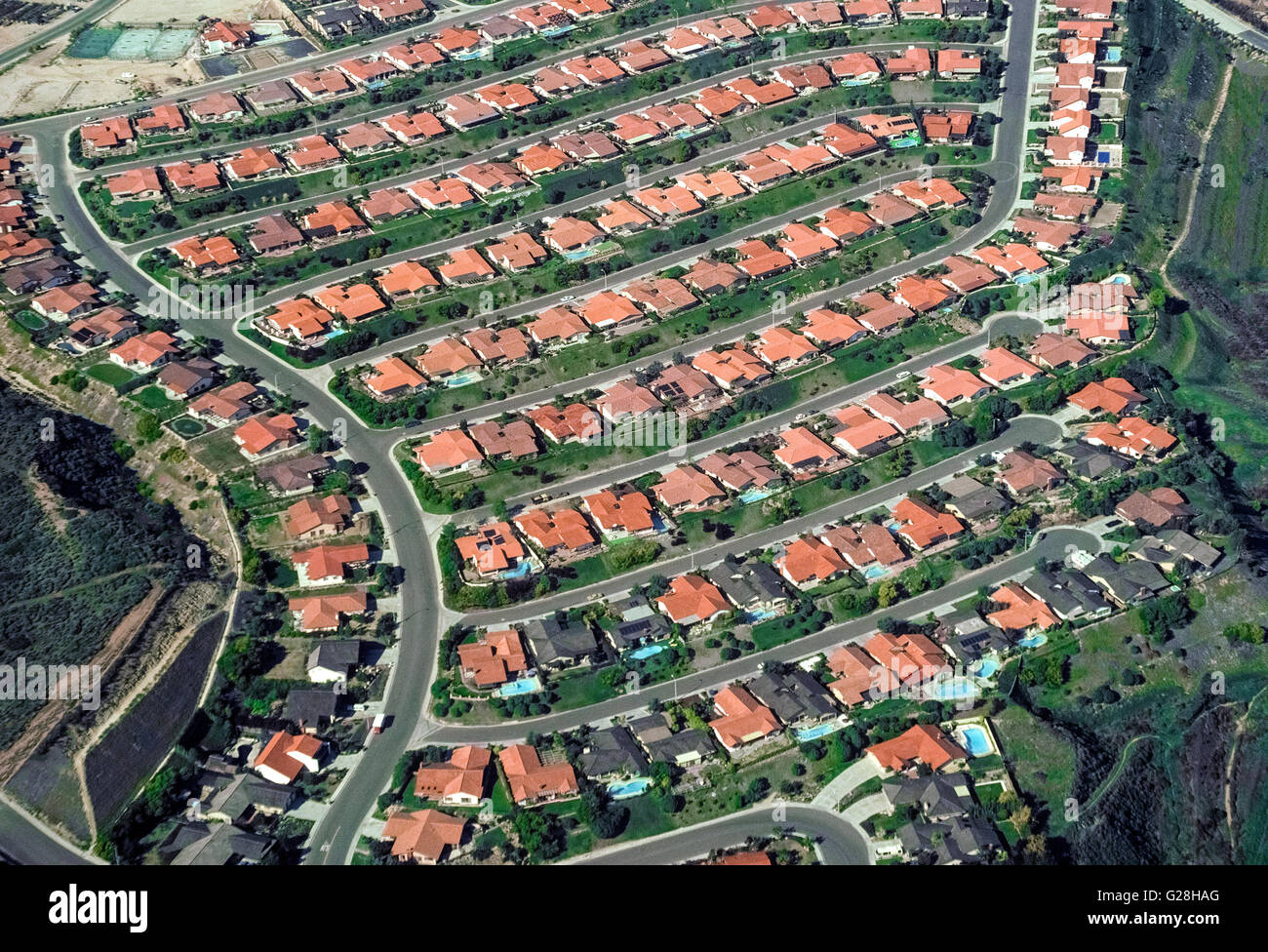 An aerial view shows side-by-side homes with red-tile roofs that are crammed into this housing development among foothills in San Diego County in Southern California, USA. Such jam-packed suburban neighborhoods are common there because of the popularity of that southernmost county in the state and the area's exceptionally pleasant weather. Stock Photo