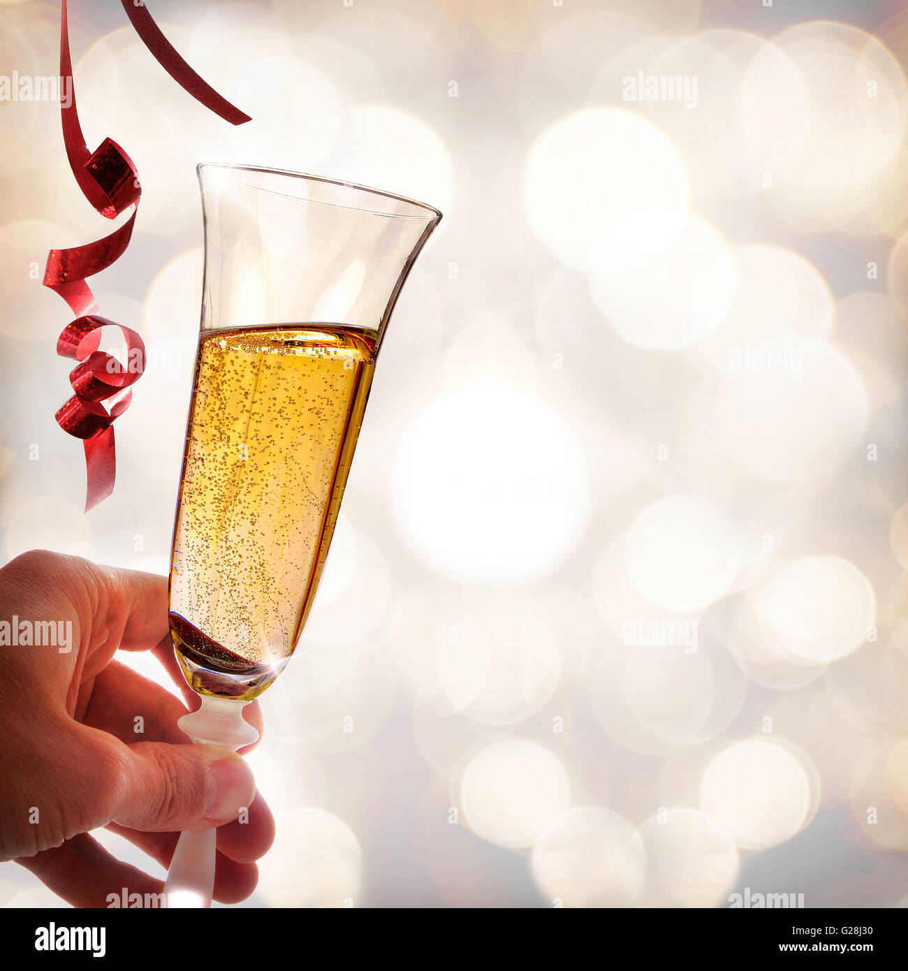 Hand holding a glass of sparkling white wine with bokeh background. With red ribbons hanging . Party concept. Square composition Stock Photo
