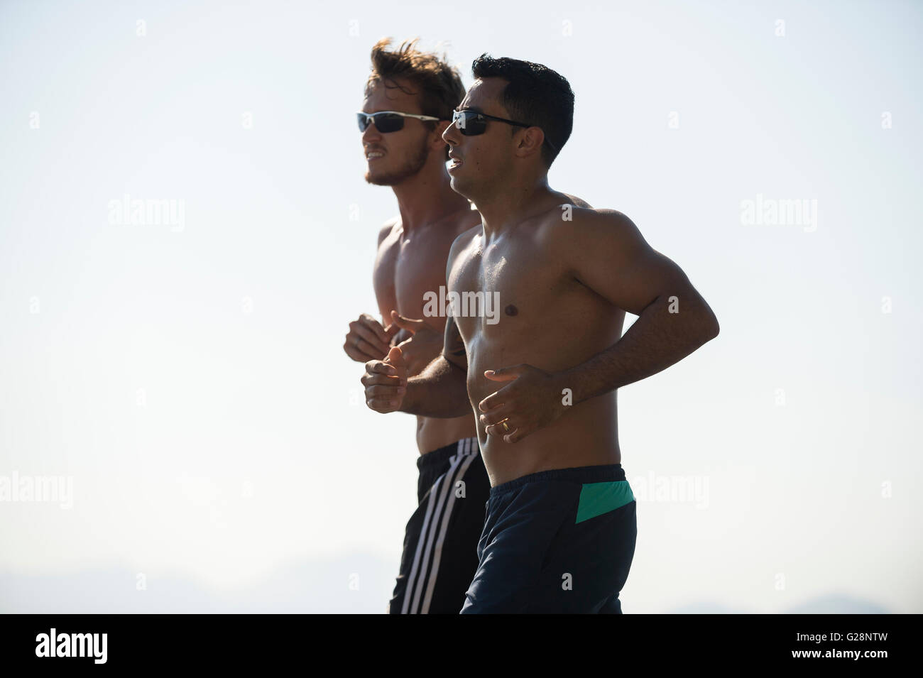 RIO DE JANEIRO - APRIL 3, 2016: Pair of shirtless young carioca Brazilian men jog together in a city known for fitness fanatics. Stock Photo