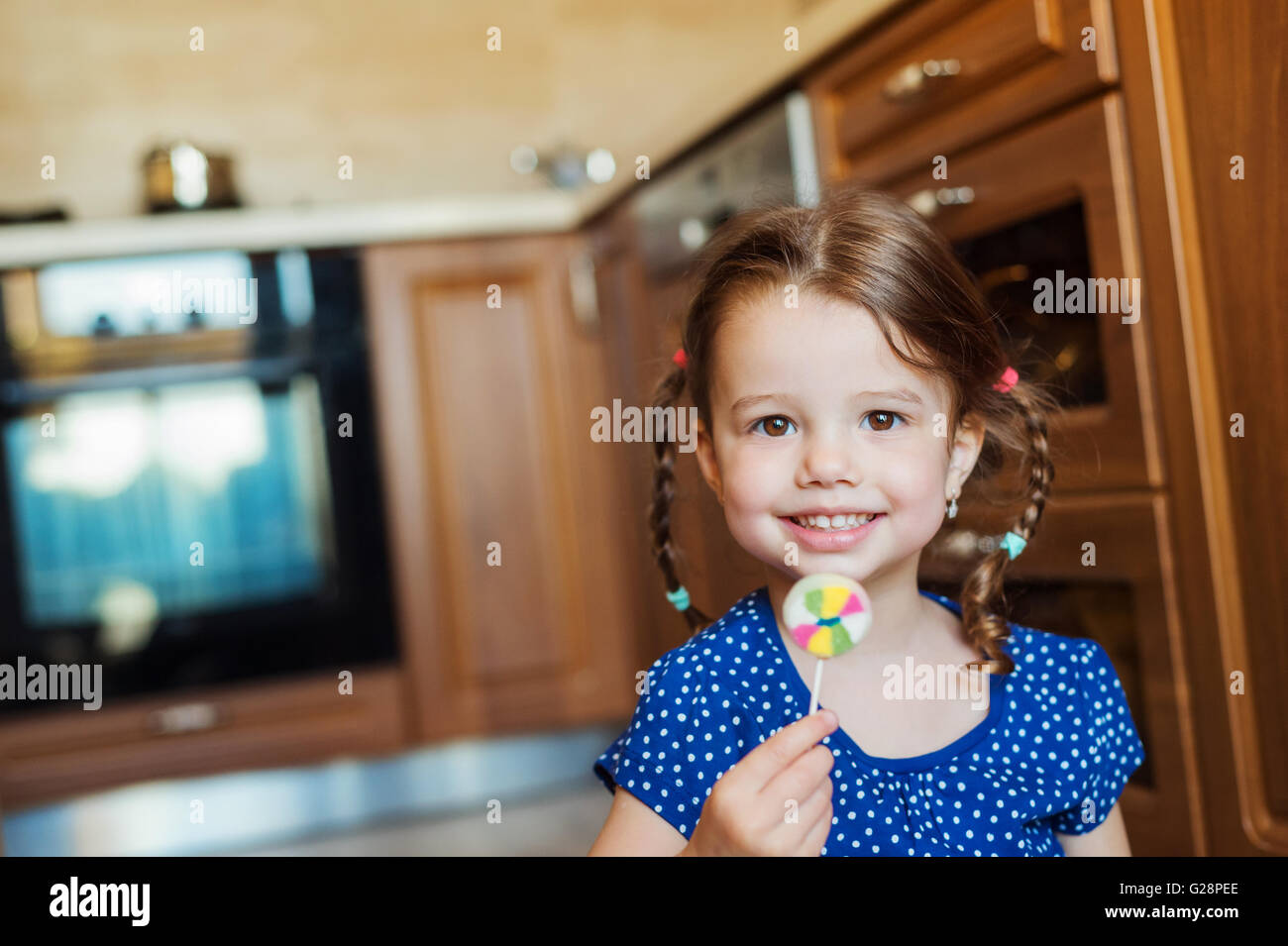 Little girl in the kitchen smiling, eating lollipop Stock Photo