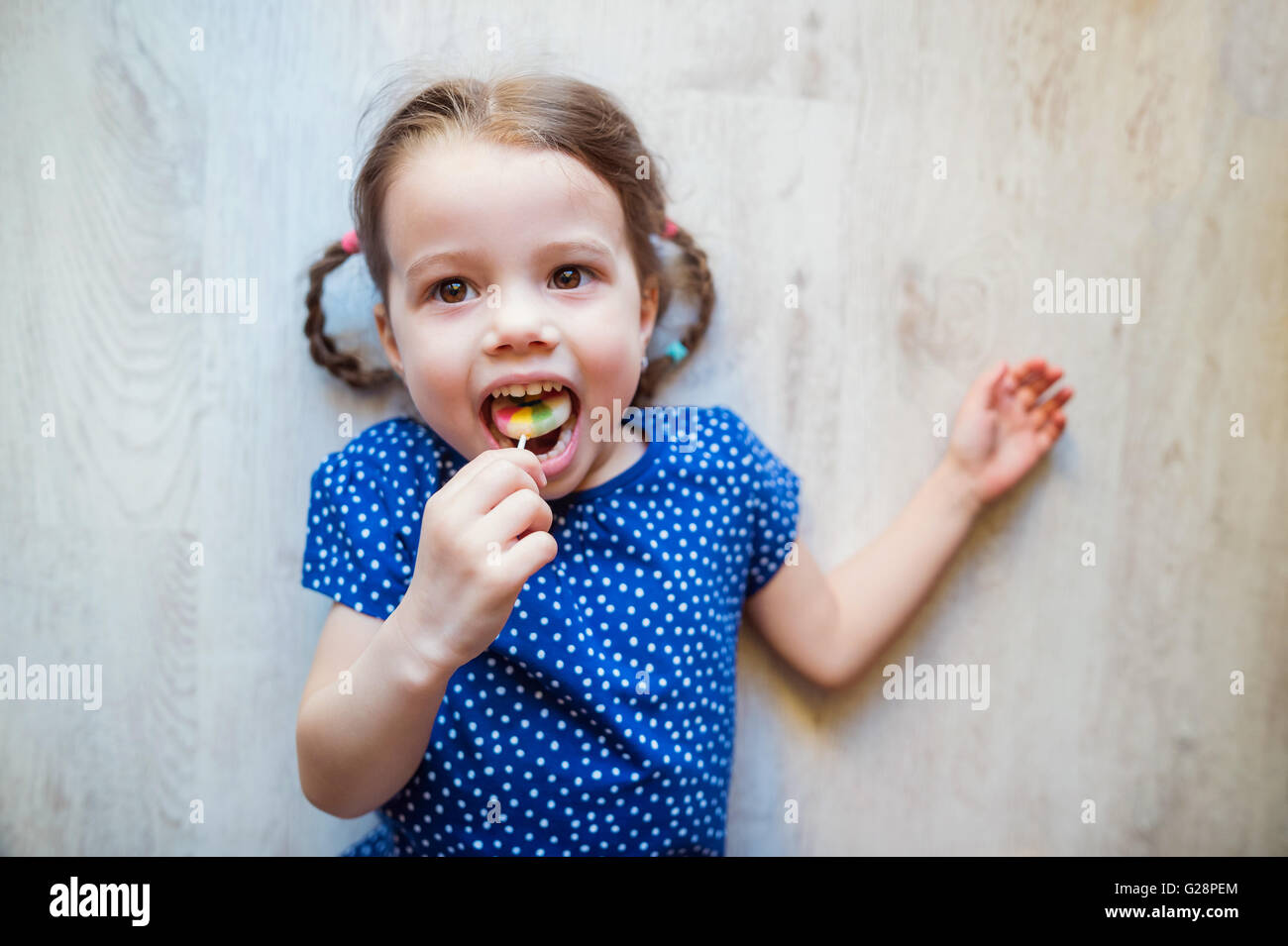 Little girl lying on the floor, smiling, eating lollipop Stock Photo