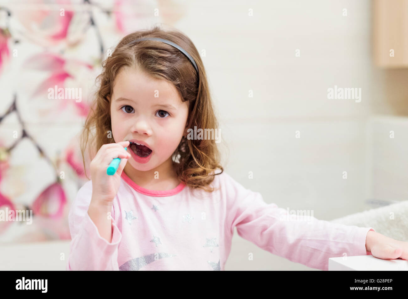 Little girl in pink pyjamas in bathroom brushing teeth Stock Photo