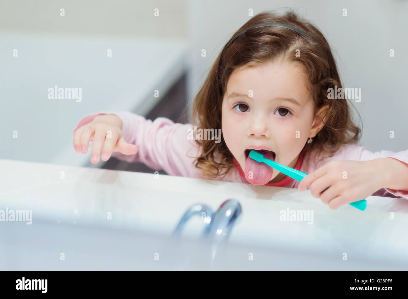 Little girl in pink pyjamas in bathroom brushing teeth Stock Photo