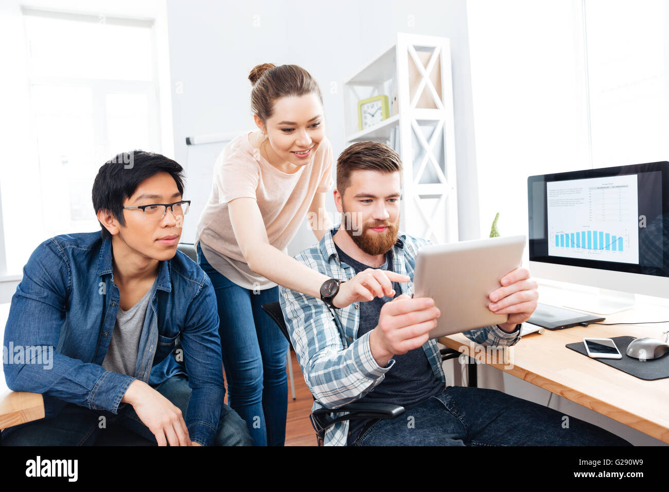 Three focused young businesspeople working in office together and using tablet Stock Photo