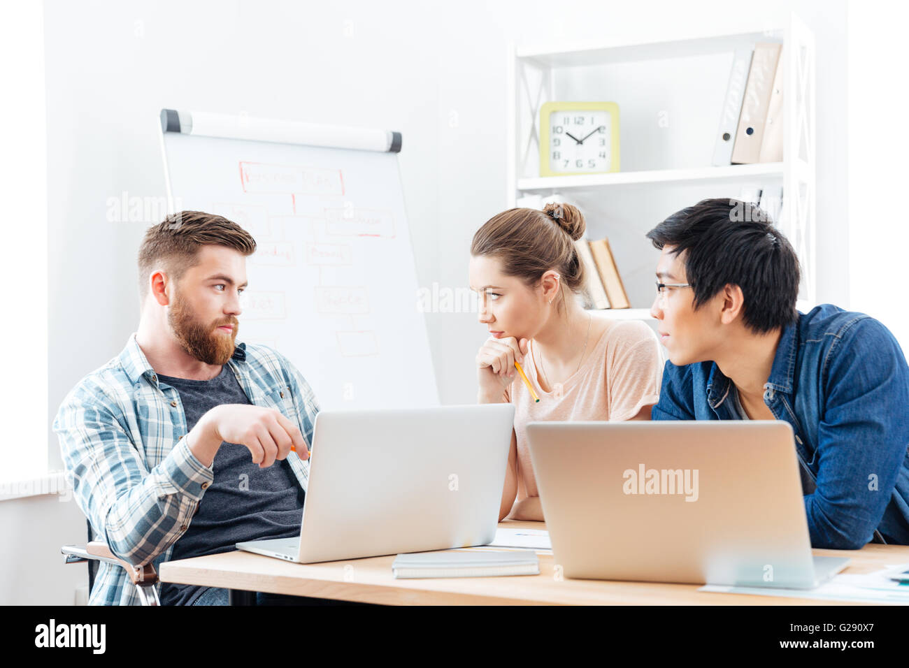 Three serious young businesspeople having a business meeting in office ...