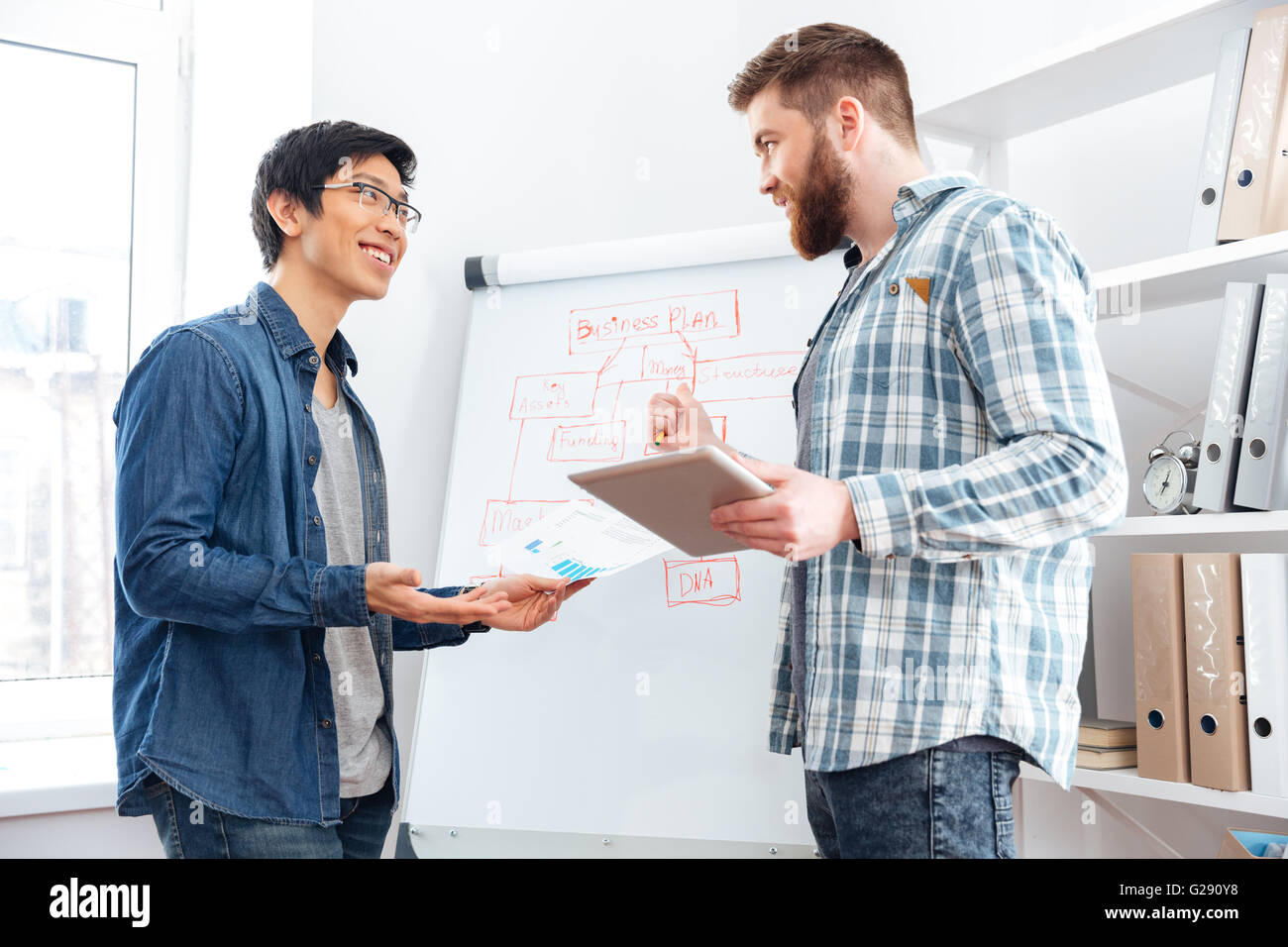 Two confident young businessmen making business plan using tablet and flipchart in office Stock Photo