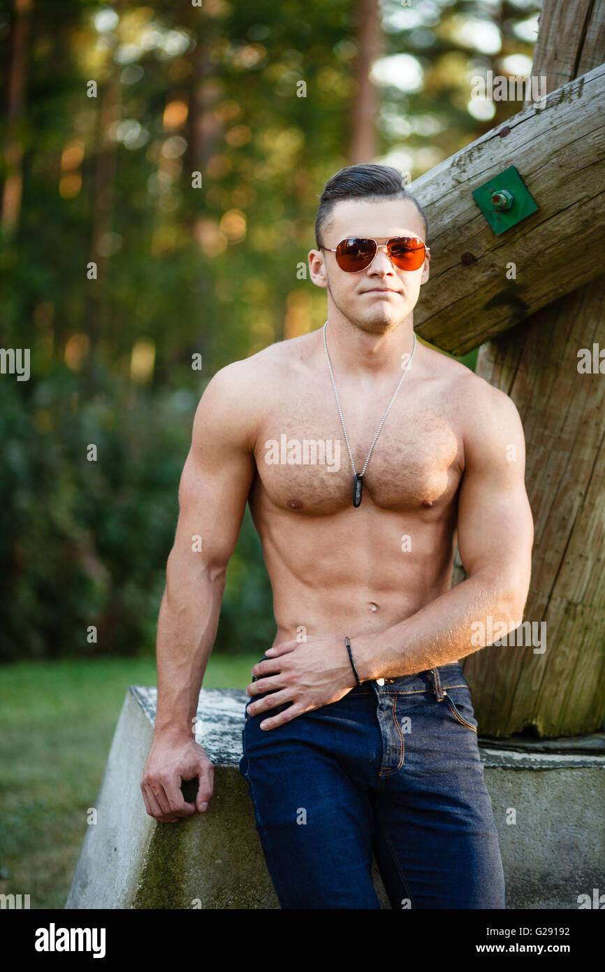 Muscular young man in sunglasses near a log. Stock Photo