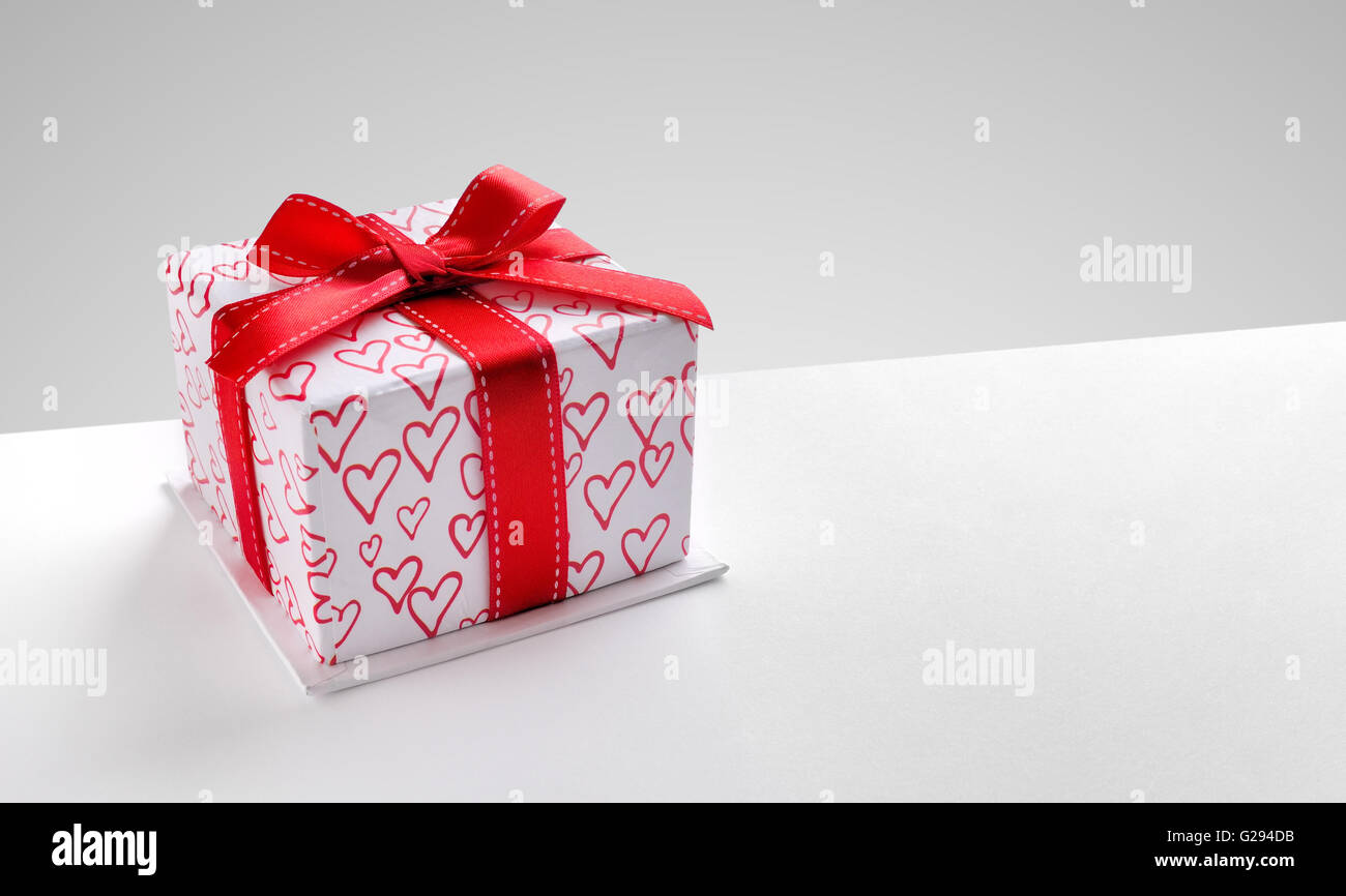 Decorative gift box with red ribbon and hearts printed on white table ...