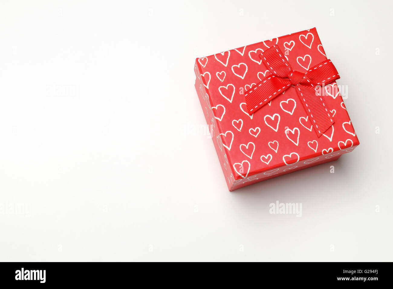 Decorative square red gift box with red ribbon and white painted hearts. Top perspective view. White isolated background. Stock Photo