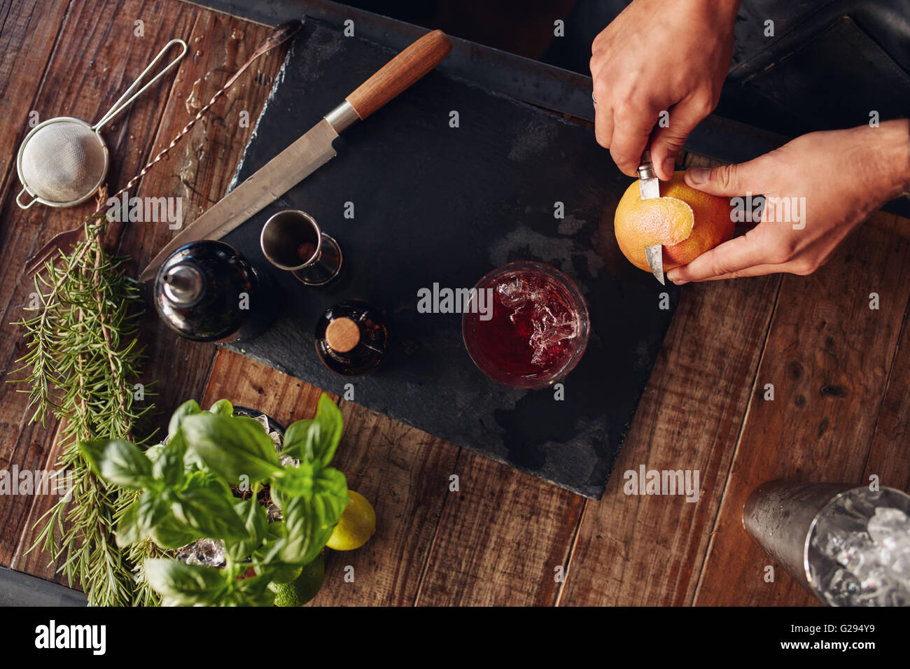Top view of bartender hands peeling off a grapefruit with cocktail glass and ingredients on table. Garnishing grapefruit cocktai Stock Photo