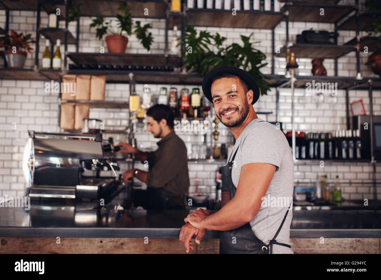 Portrait of happy young male coffee shop owner standing with barista working behind the counter making drinks. Stock Photo