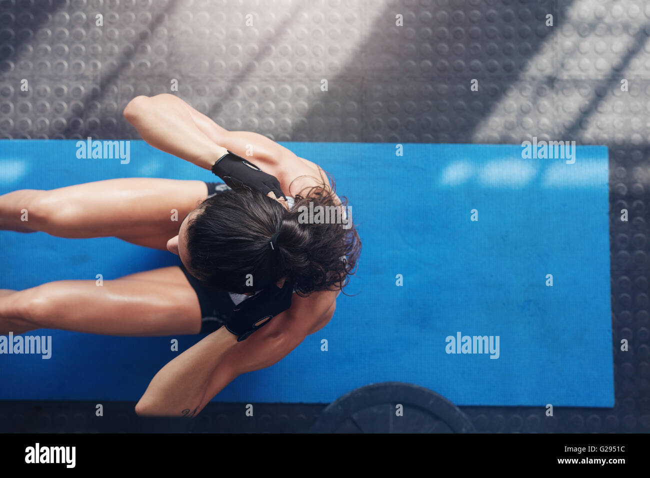 Overhead view of female working out at the gym. Muscular young woman doing sit ups on an exercise mat. Stock Photo