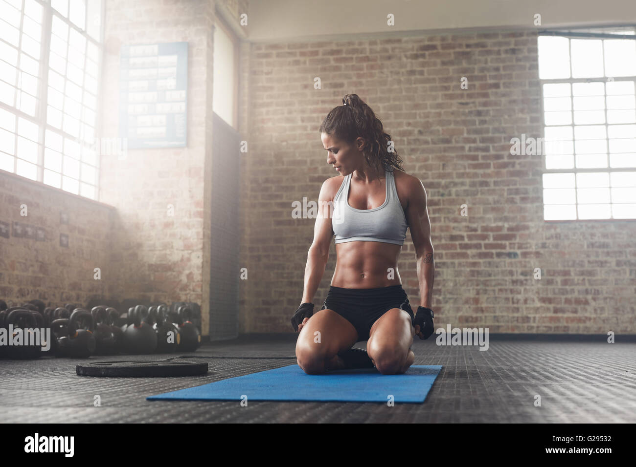 Indoor shot of fitness young woman sitting on yoga mat at gym. Muscular