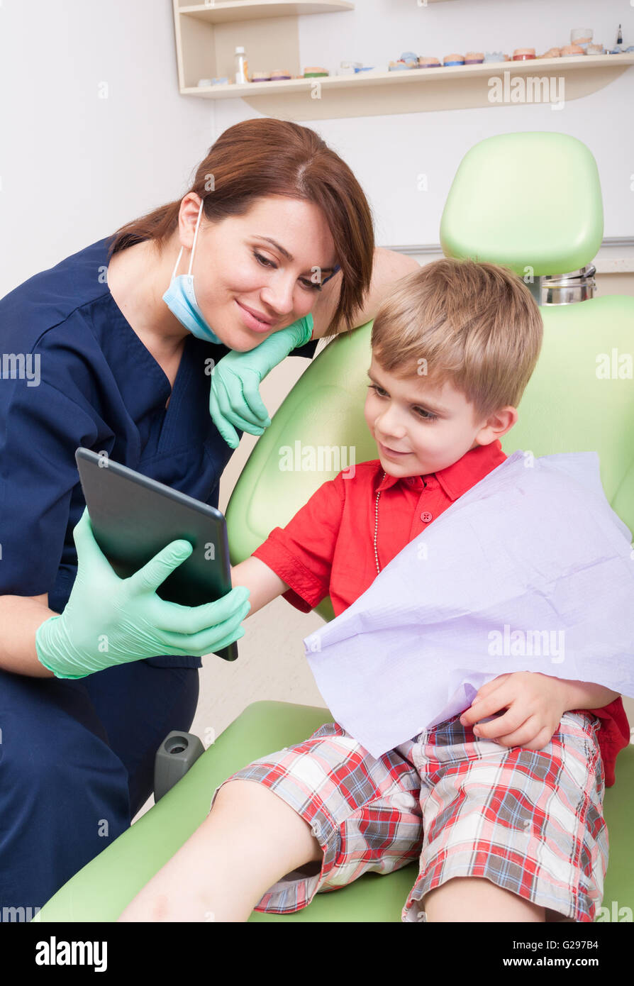 Happy kid patient at friendly woman dentist using wireless tablet to have fun and relax Stock Photo