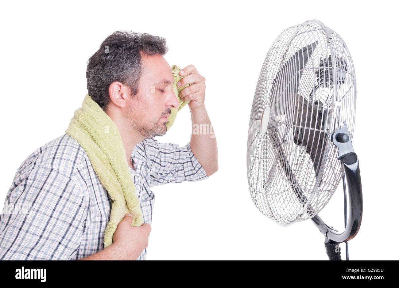 Man wiping sweaty forehead in front of cooling fan as hot summer dehydration concept Stock Photo