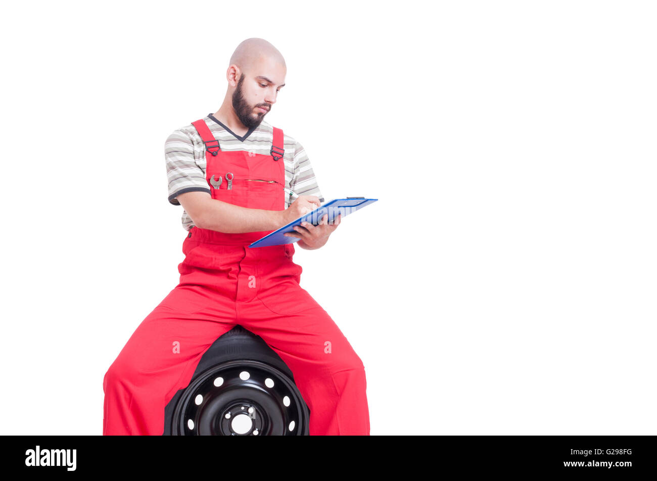 Mechanic writing on clipboard while sitting on car wheel isolated on ...