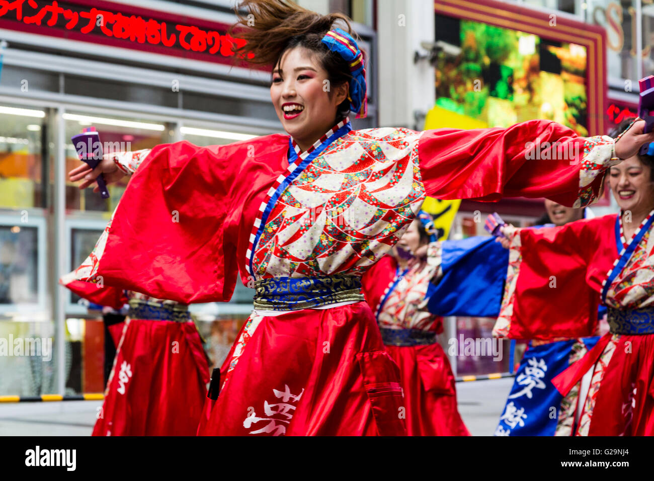 Japan, Kumamoto. Hinokuni Yosakoi dance festival. Close up of Japanese young woman dancer, part of a team, arms outstretched, dancing in mall. Stock Photo